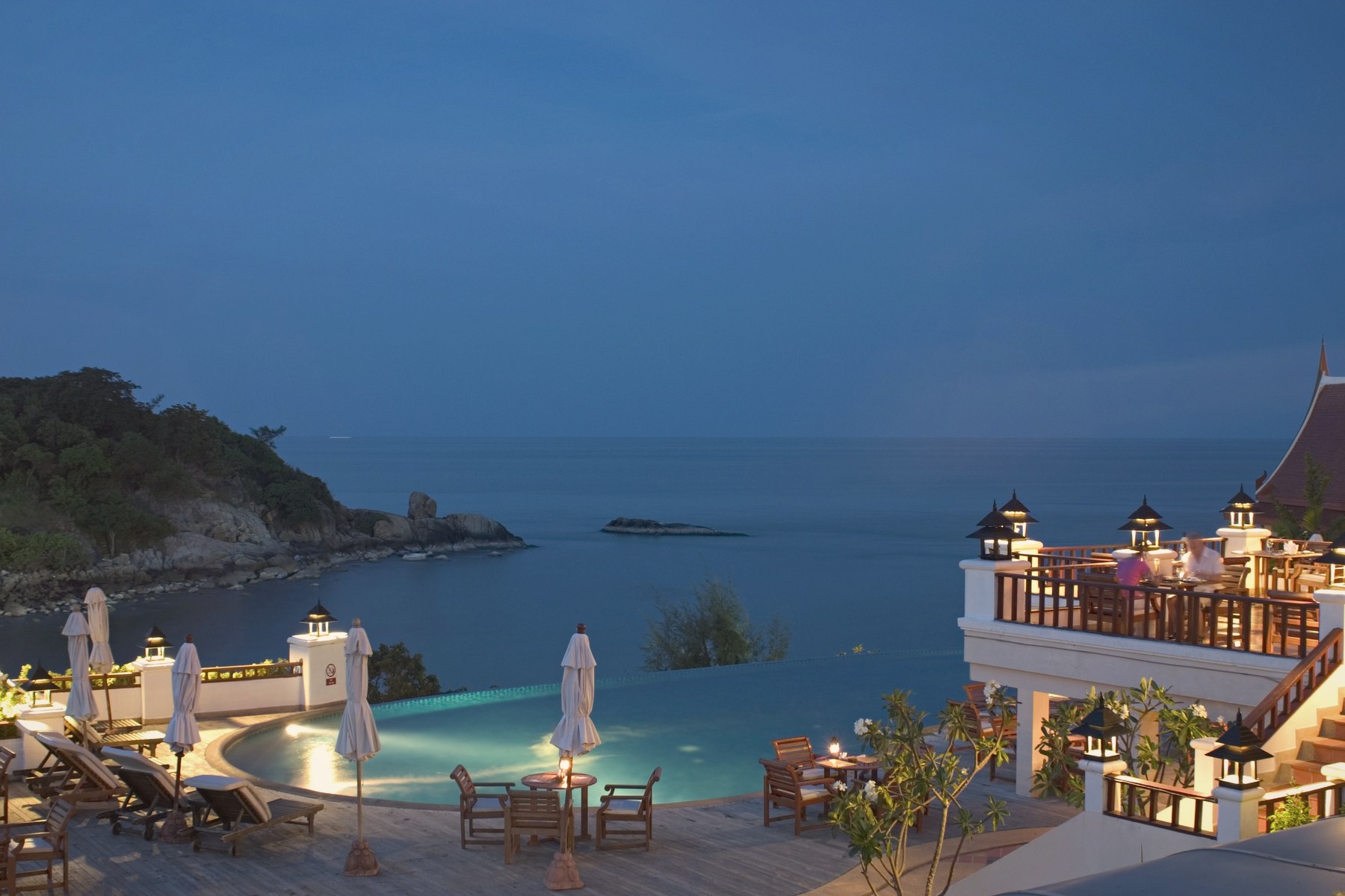 A lantern-lit pool terrace over the sea at dusk