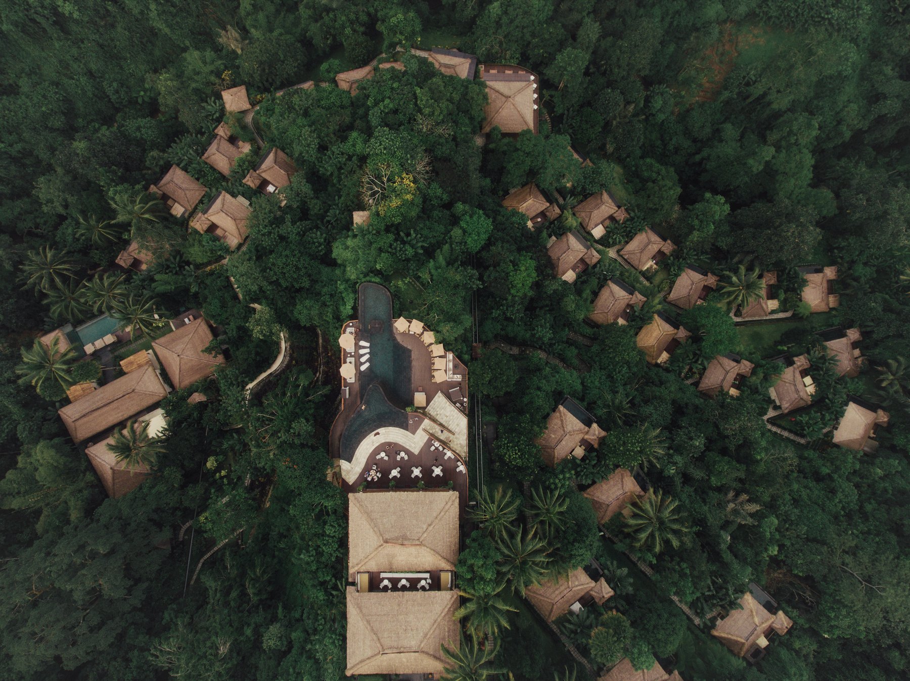 An aerial view of a thatched-roof resort tucked into dense jungle canopy