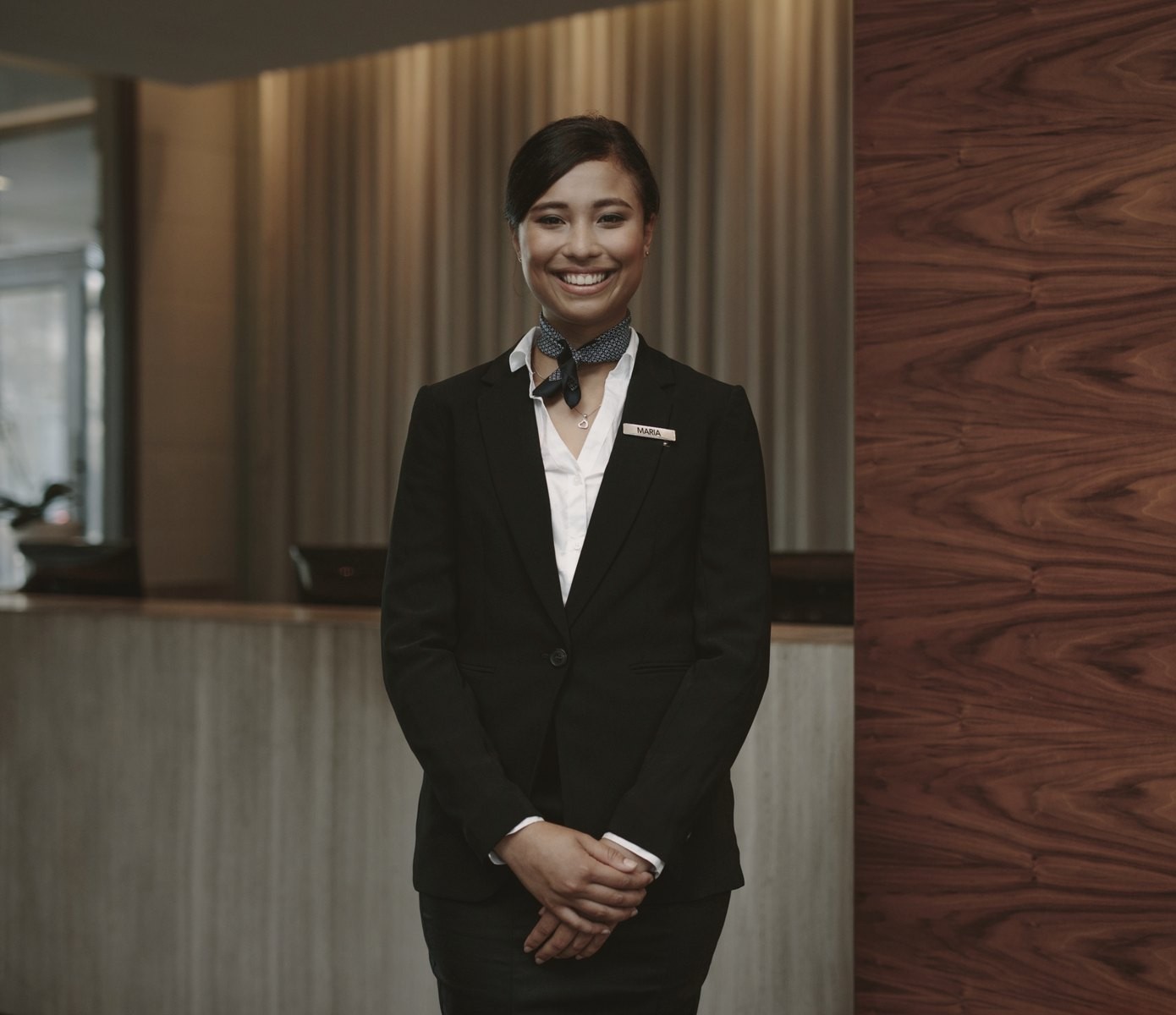 A smiling hospitality host in a tailored suit at a warm timber reception